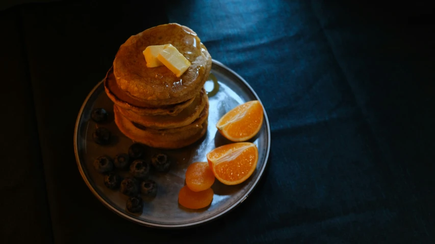 pancakes are stacked on a plate with blueberries and orange slices