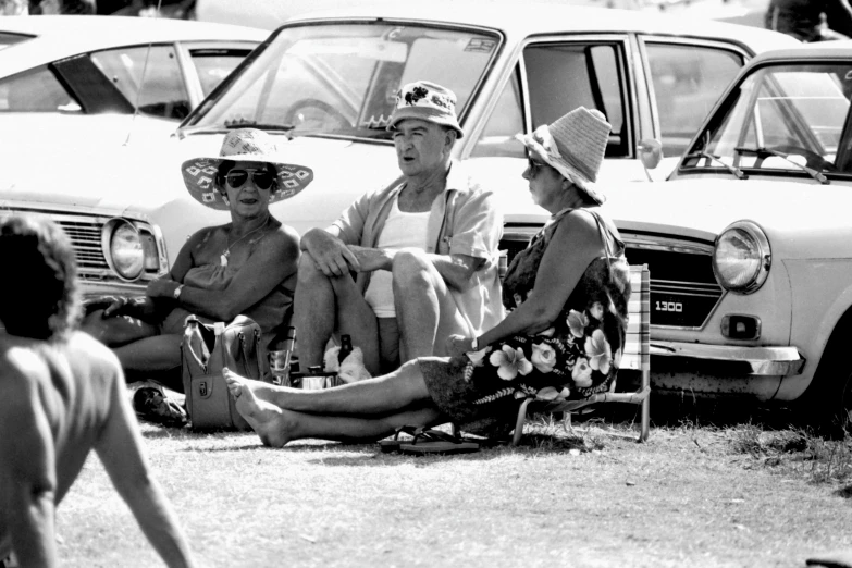 two people sitting on a chair at a car show