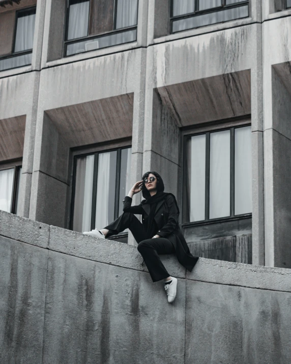 man wearing black leaning up against wall on cellphone