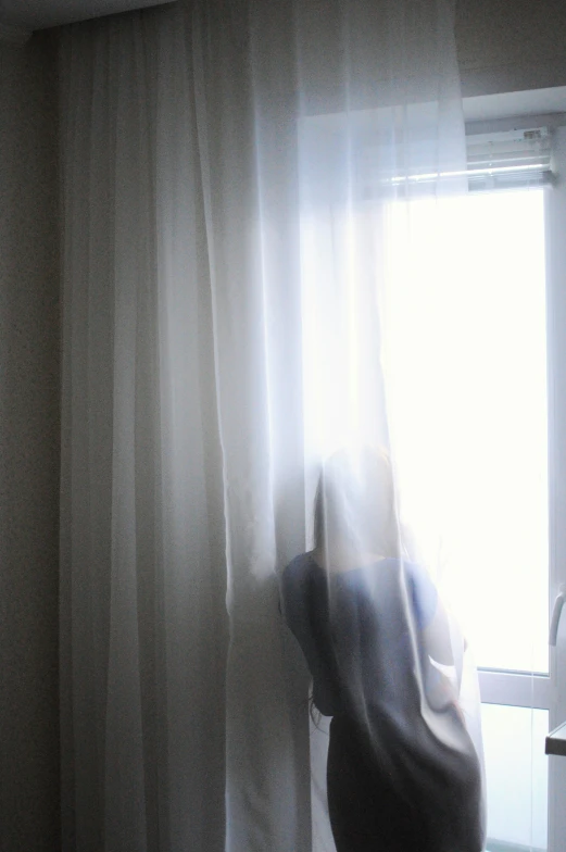 the woman is standing near a window in her bedroom