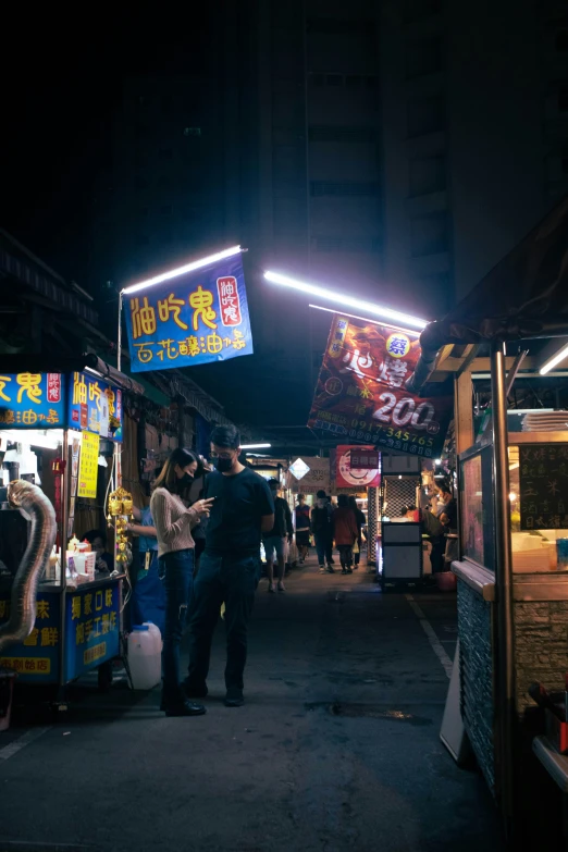 a street with people standing at night looking at a vendor stand