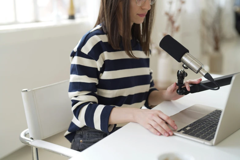 a woman sitting in front of a laptop computer holding a microphone