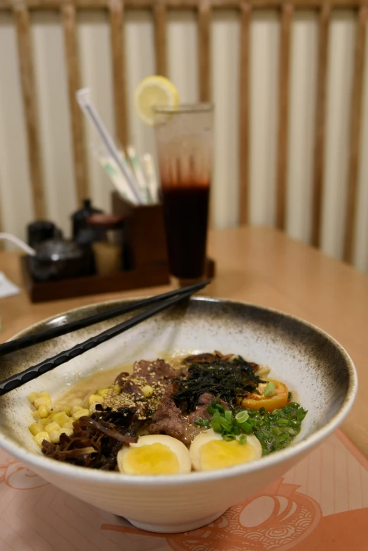 a bowl of noodles and meat with chopsticks on a table