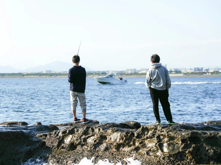 two men are fishing in the water off a rock wall