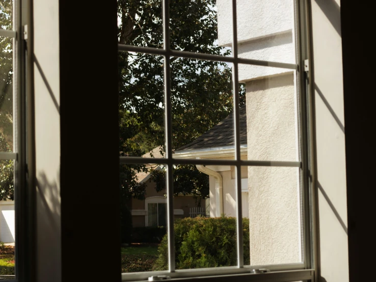 an open window shows a white building with a roof and trees