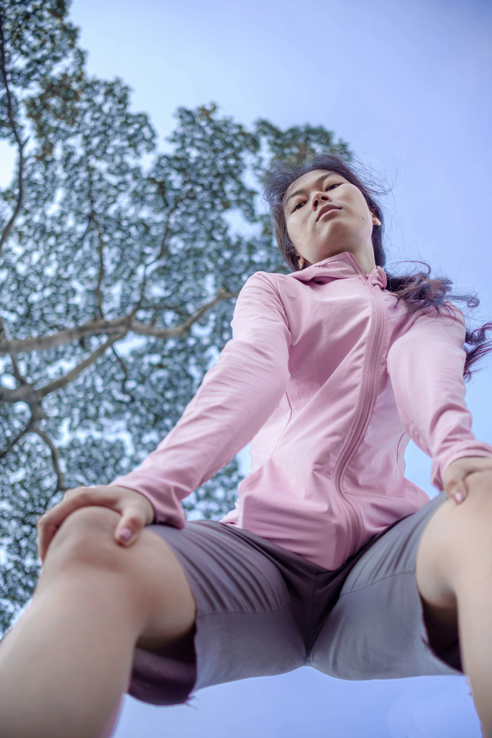 a young lady is sitting on the ground in front of a tree