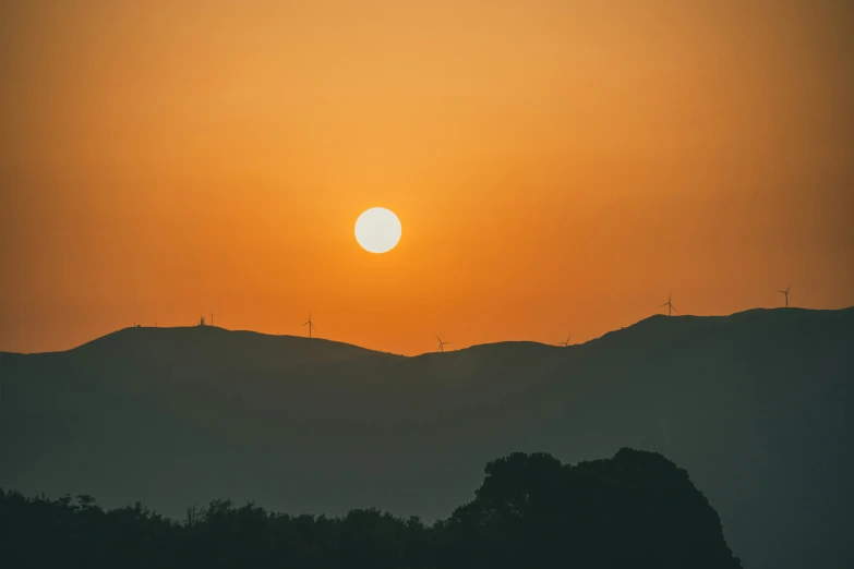 a sunset on a mountain with a silhouette of hills