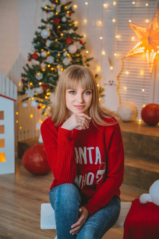 a woman wearing a red christmas sweater posing for a portrait in front of a tree