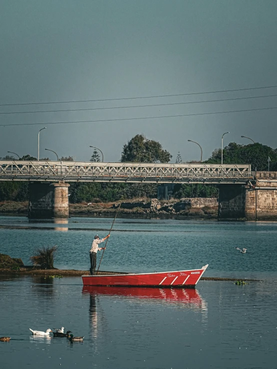 the man is standing in a small red boat in the water