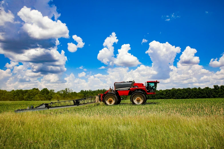 a red farm vehicle traveling through a grassy field