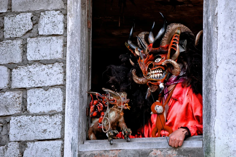 three horned devil mask heads are seen from an opening in a wall