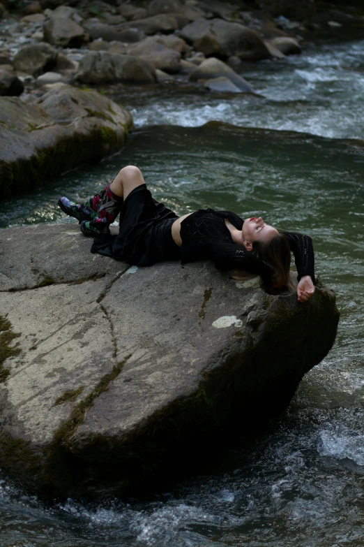 woman lying on rock in river next to rocks