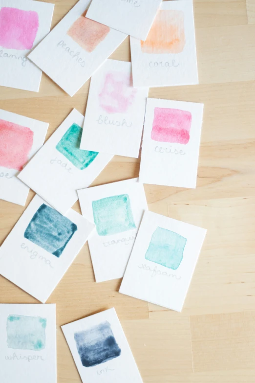 nine swatches of watercolor sitting on top of a wooden surface