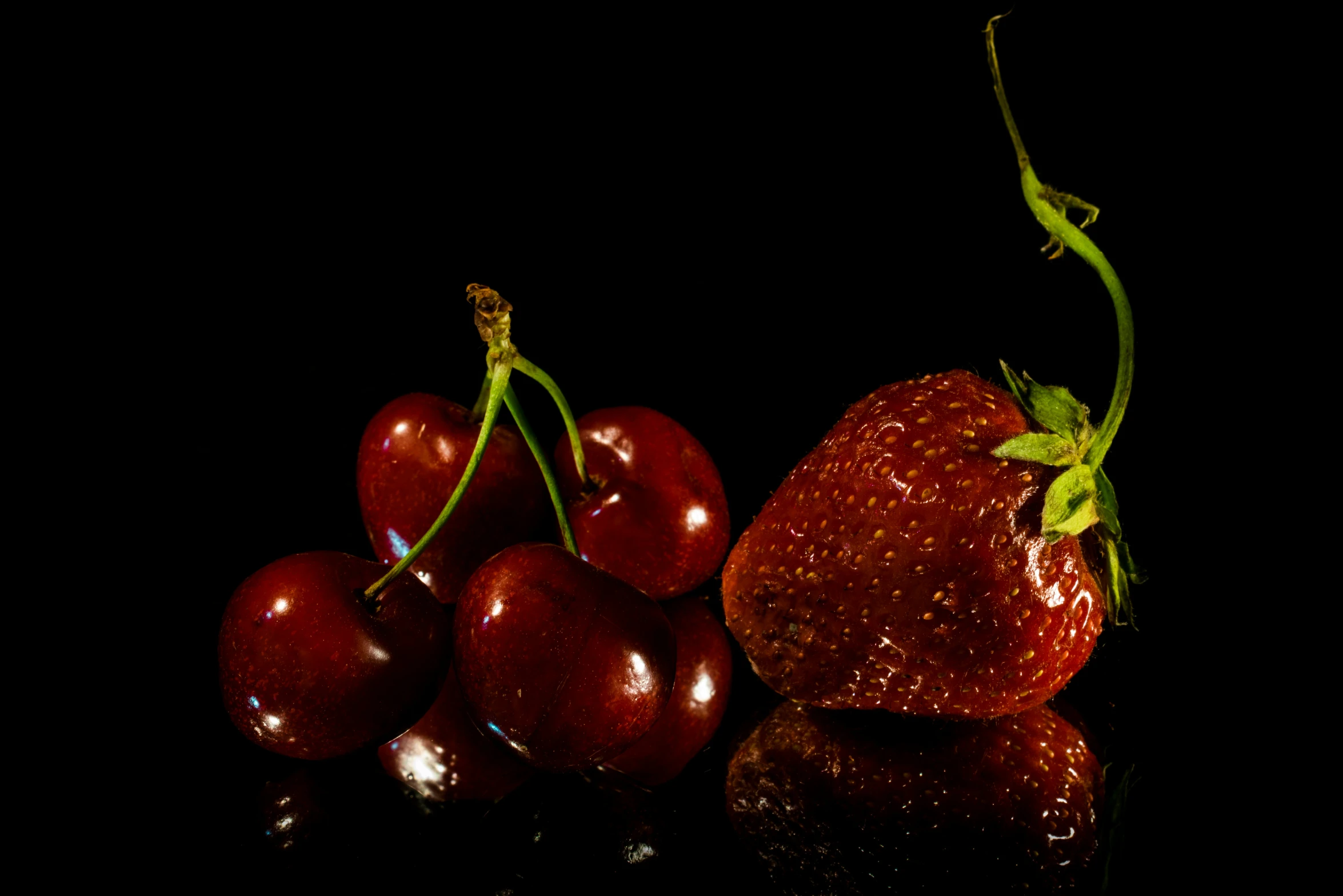 some red fruit and a single strawberry on a black surface