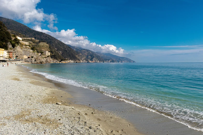 an empty beach with blue water next to a hill