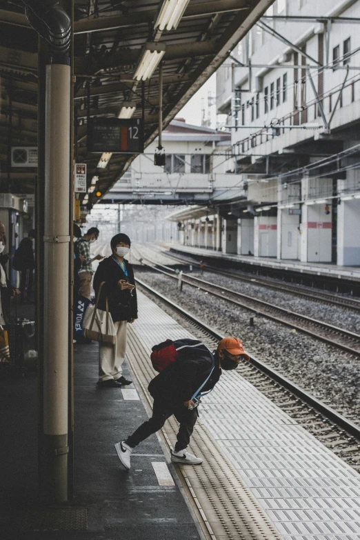 people wearing masks stand on train tracks at an outdoor train station