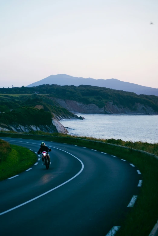 a person is riding on the side of a curved road near a bay