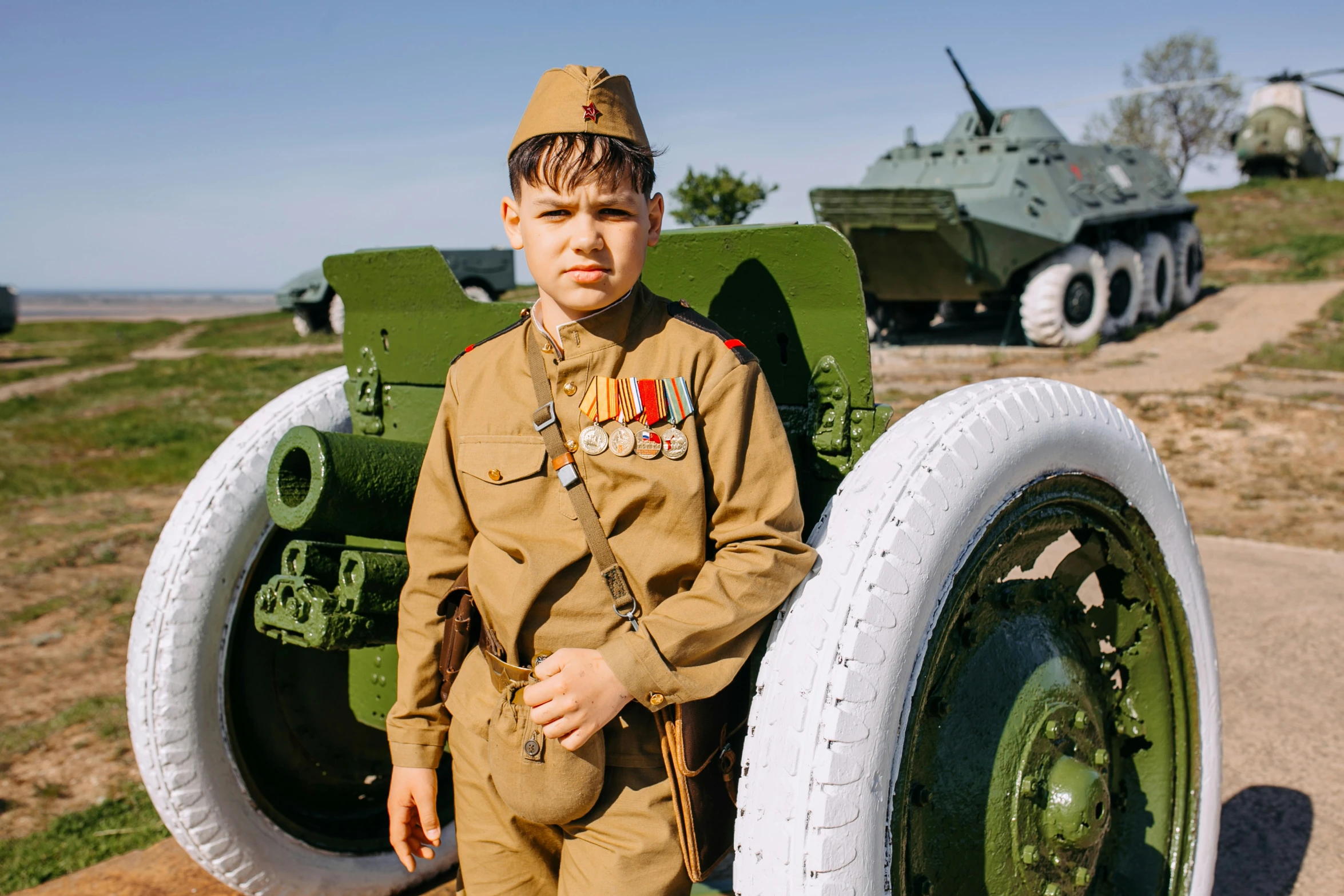 a boy in a soldier uniform stands next to some army vehicles