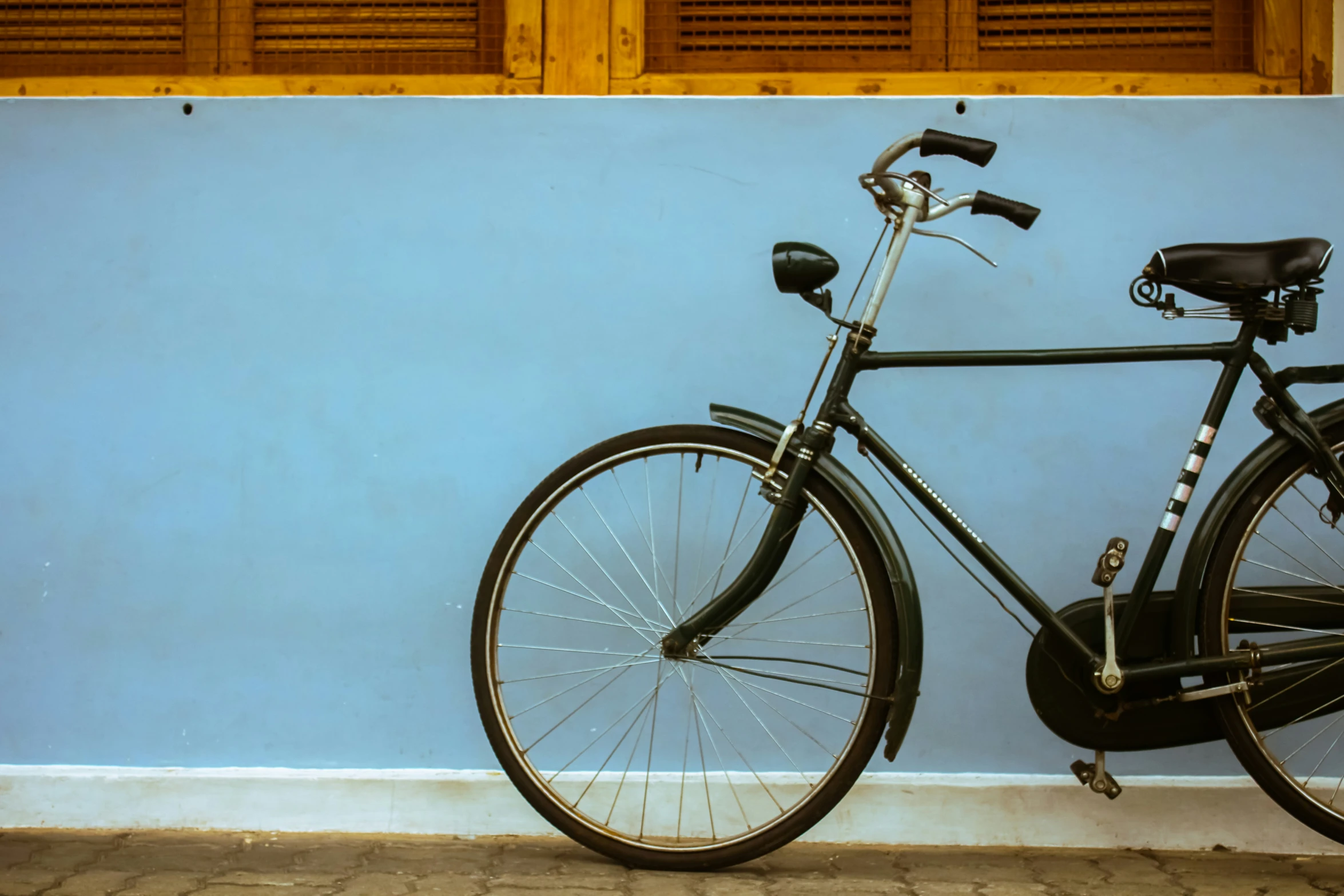 a bicycle leaning against a blue wall and two wooden shutters