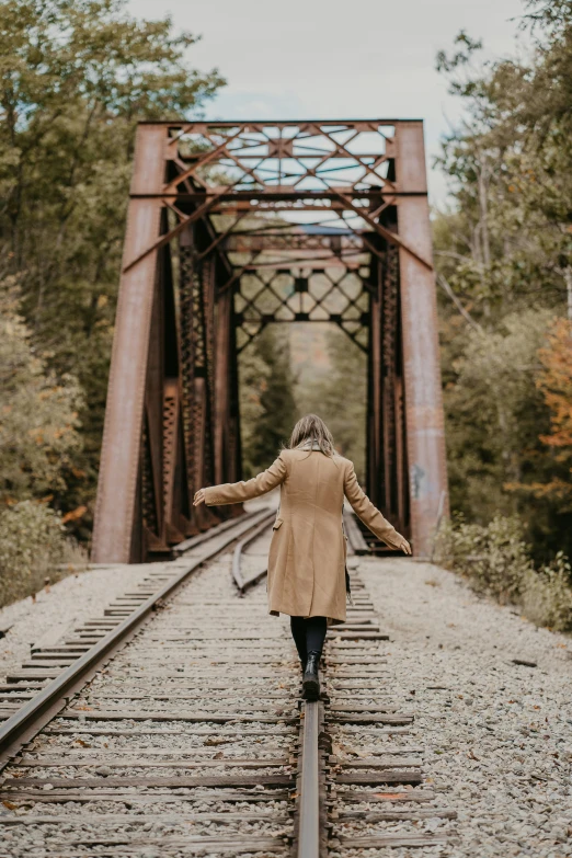 a woman wearing a tan coat is crossing railroad tracks