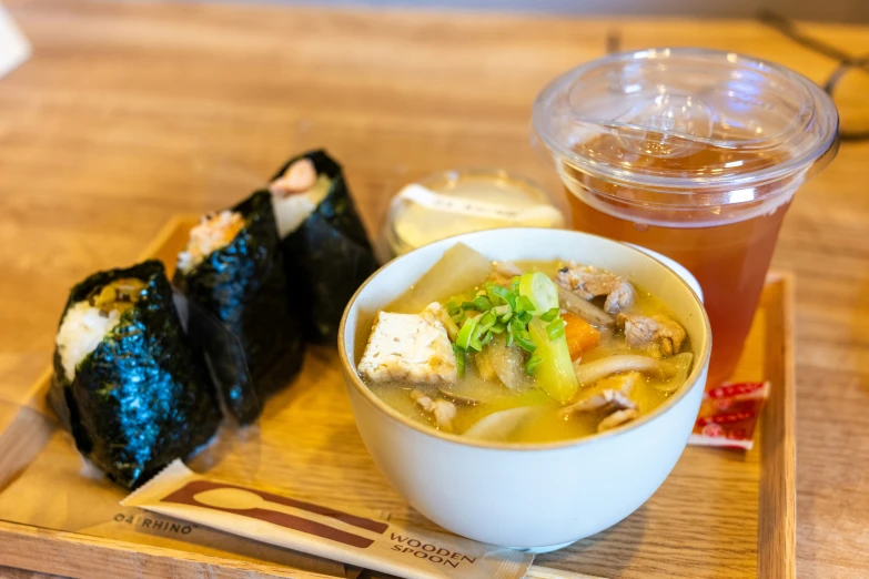 there is a small bowl with soup and a side of sushi on a tray