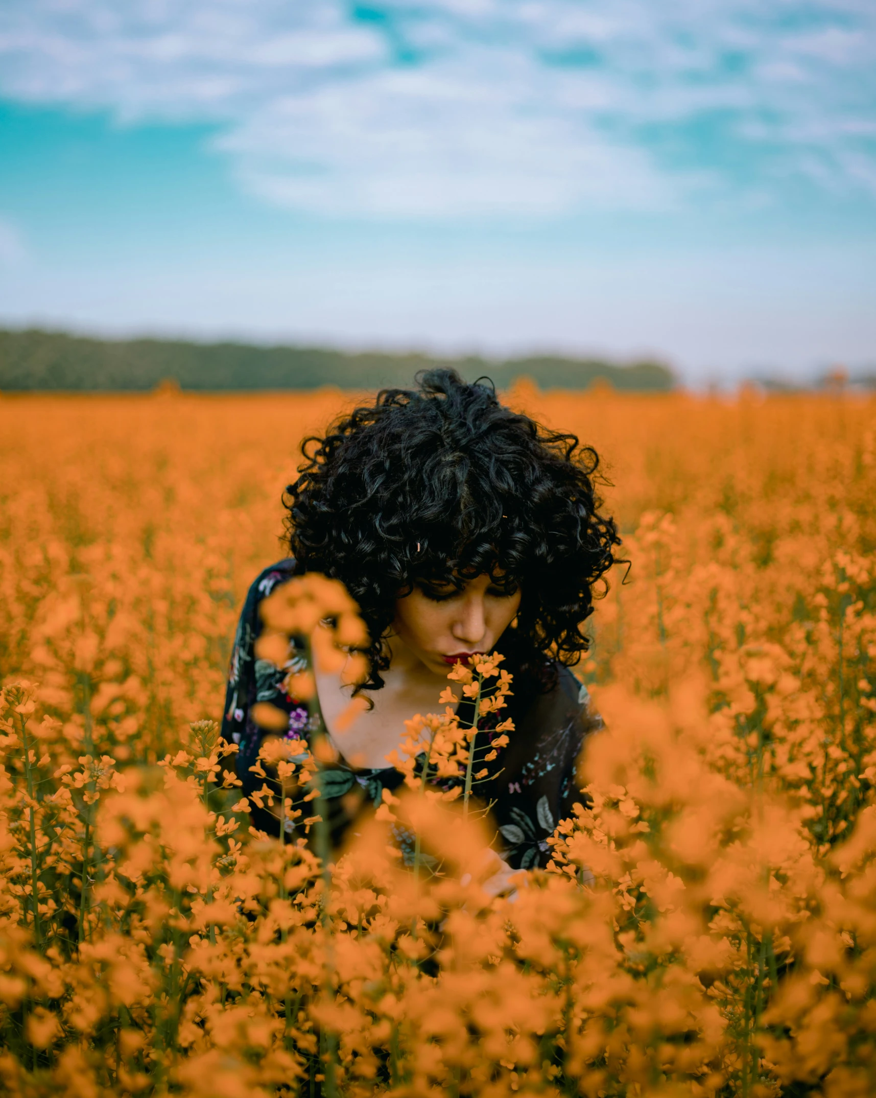 young woman with curly hair standing in a field of tall flowers