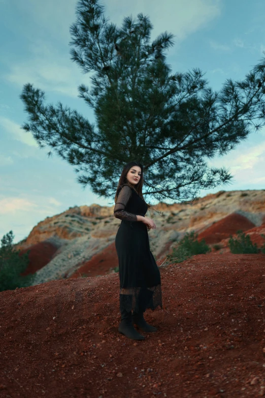 woman in black dress standing near tree and red hillside