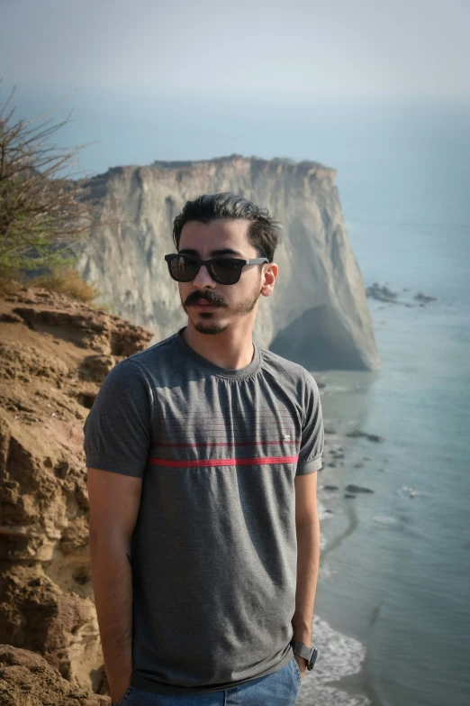 a man wearing sunglasses stands on a cliff next to the ocean
