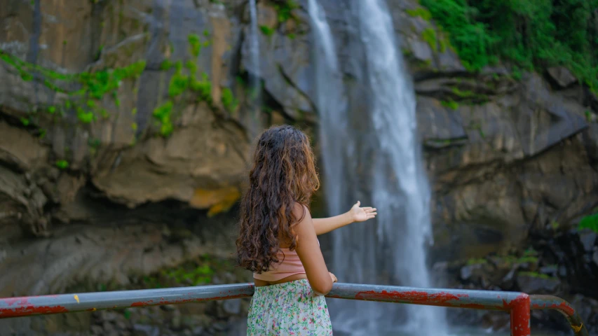 girl standing near waterfall pointing her finger at the waterfalls