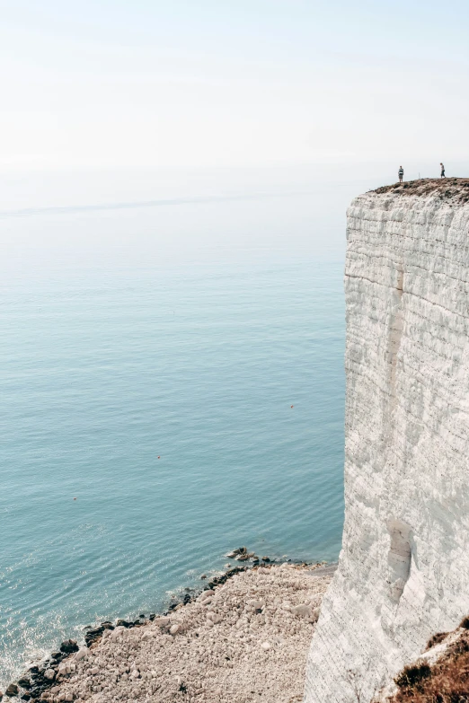 some people are sitting on top of the cliff overlooking the ocean