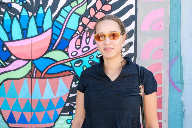 a woman in sunglasses poses next to colorful painting