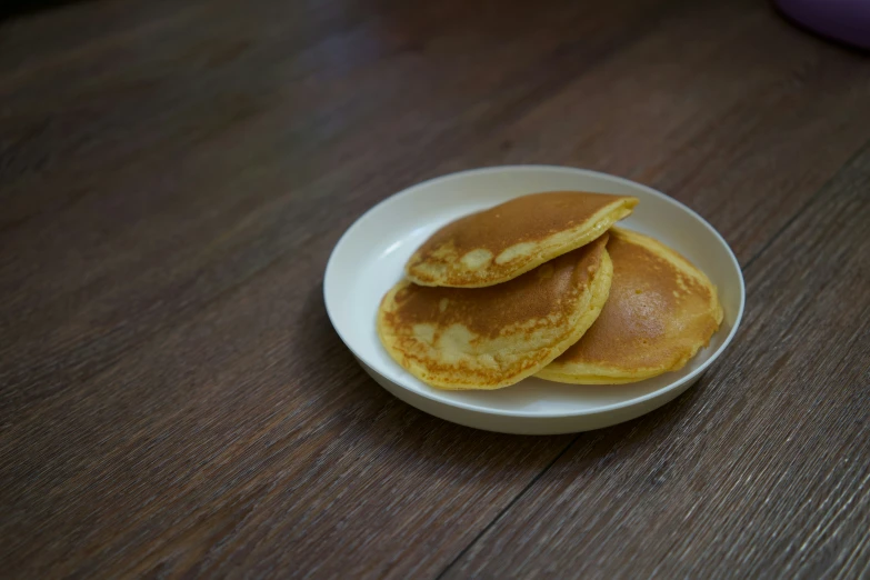 three small pancakes on a white plate on a wooden surface