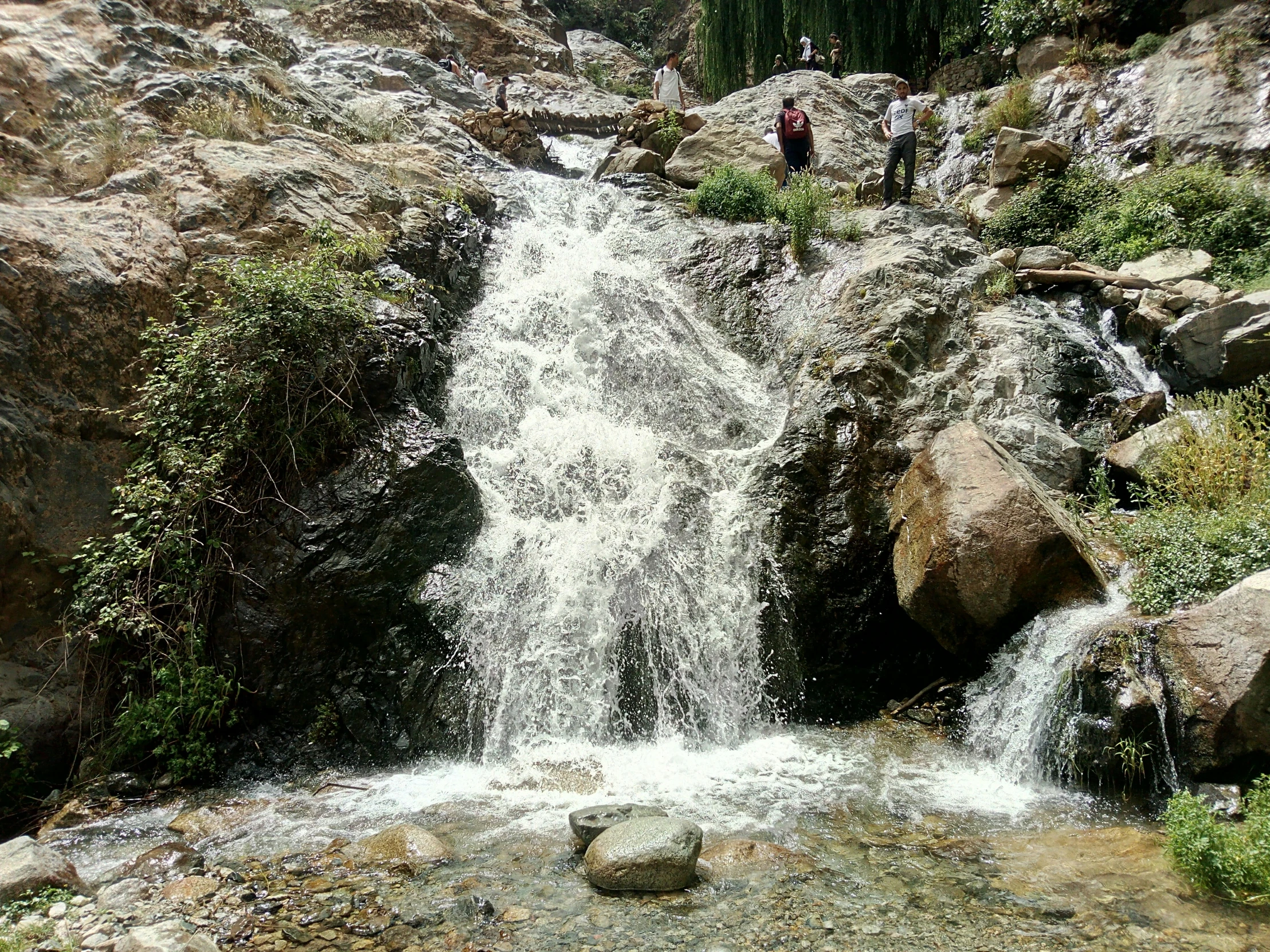 two people are near a waterfall in the mountains