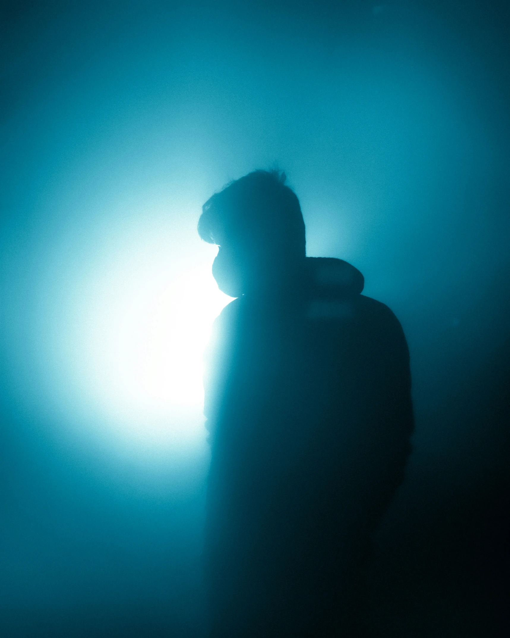 a person standing alone in the dark with his head obscured by light