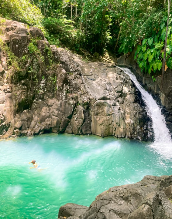 man swimming in blue lagoon next to waterfall