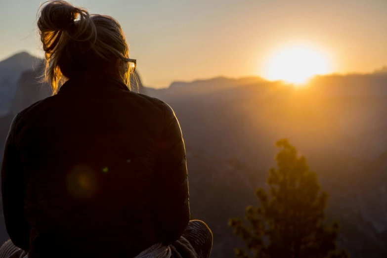 a woman sitting at the top of a hill watching the sun go down