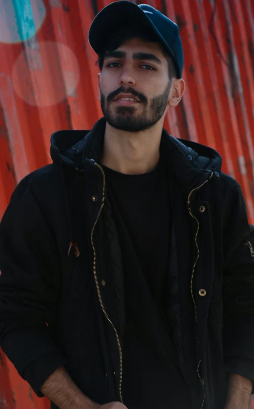 a man with a beard wearing a hat, standing near red and green graffiti