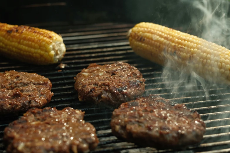 hamburgers are cooking on a grill with corn