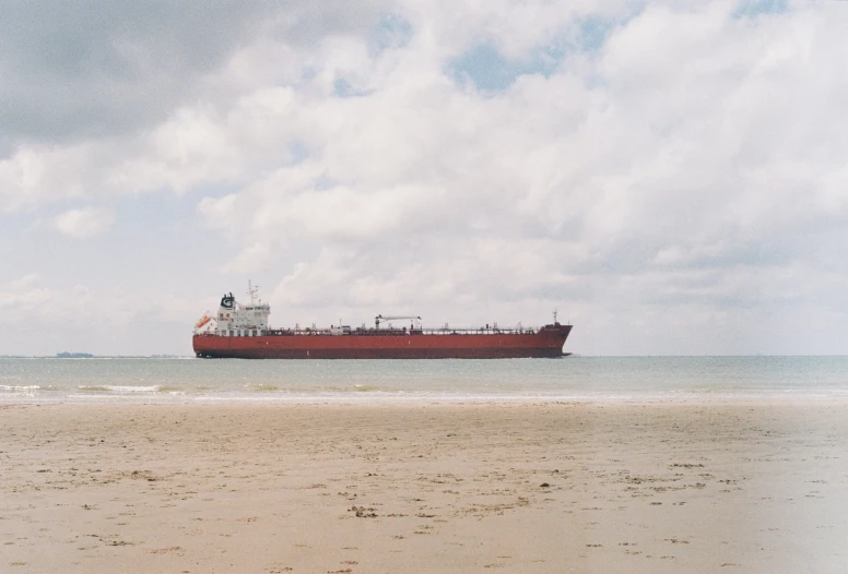 a large red ship in the ocean and some sand