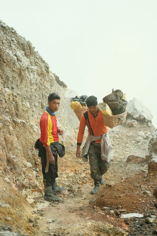 two men carry large bags while climbing a steep hill