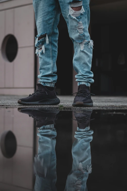 a man with ripped blue jeans and black shoes standing in front of a water dle