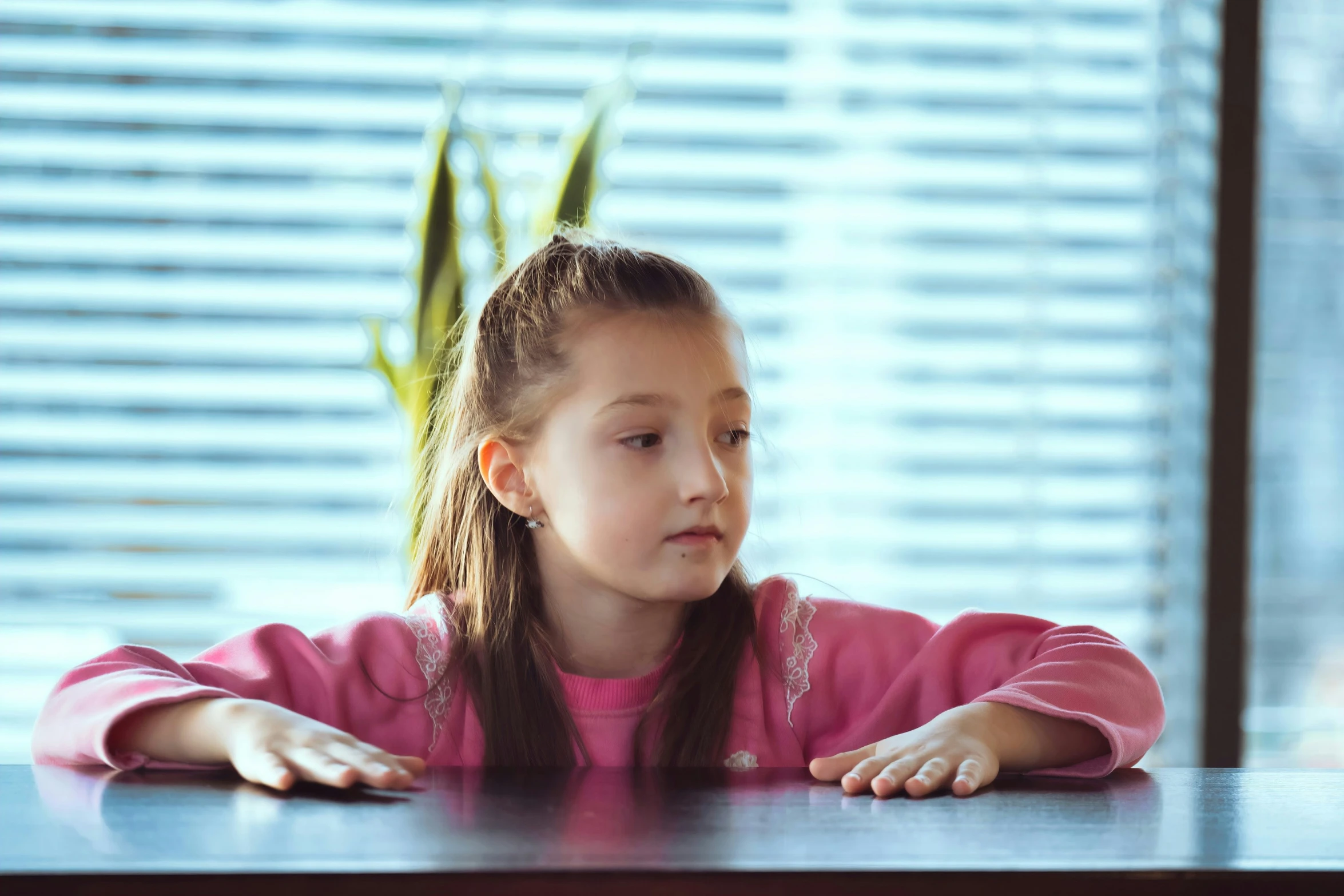 a girl sitting at a table staring out of the window