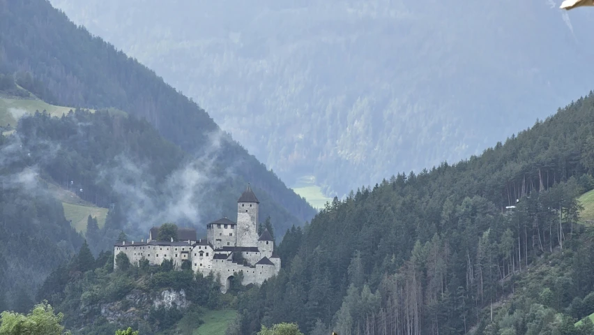 a castle surrounded by forest and mountains in the background