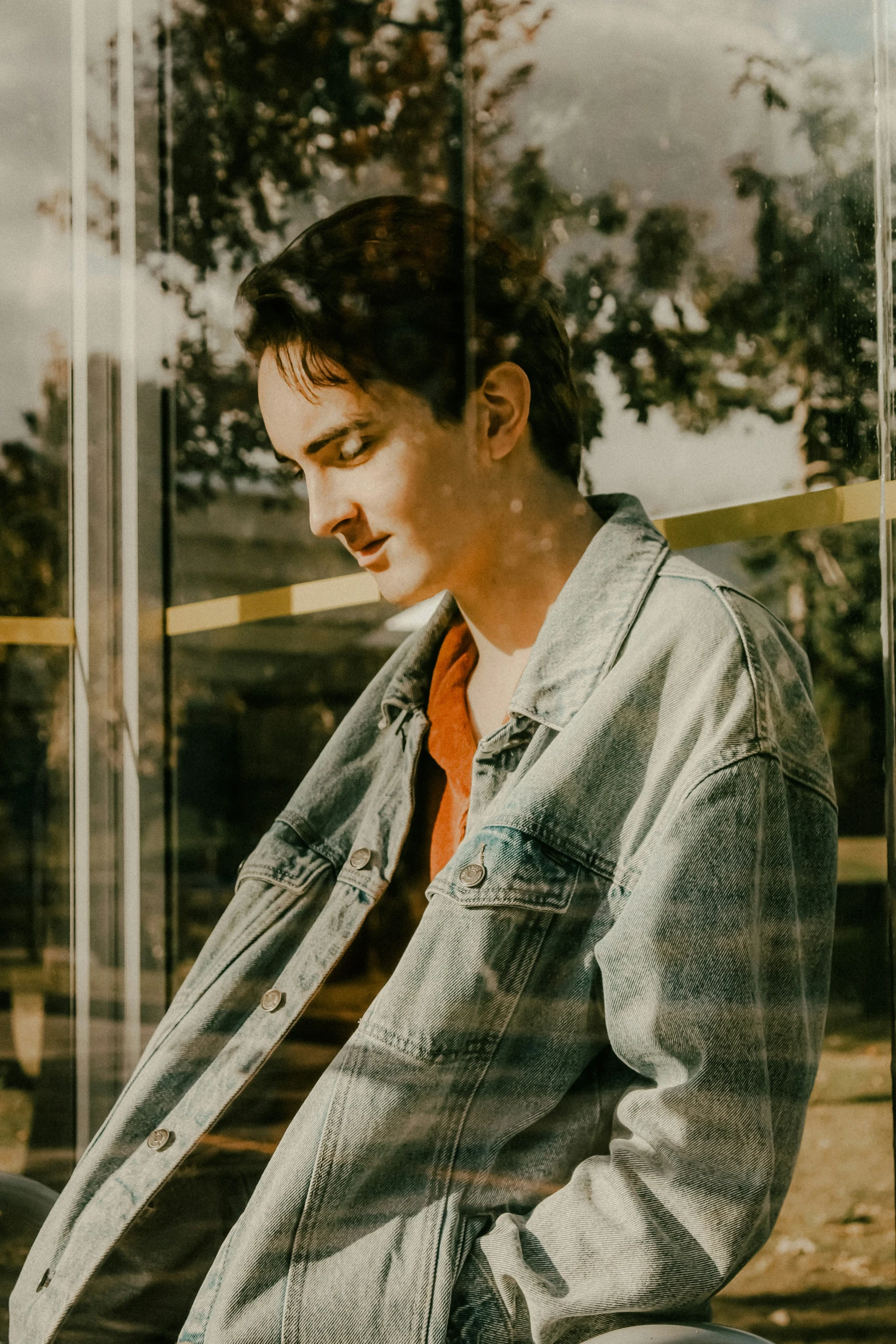 a young man sits inside of a glass front window while looking at his phone