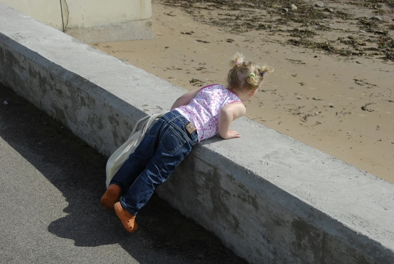 a little girl is leaning on concrete ledges to look at the ground