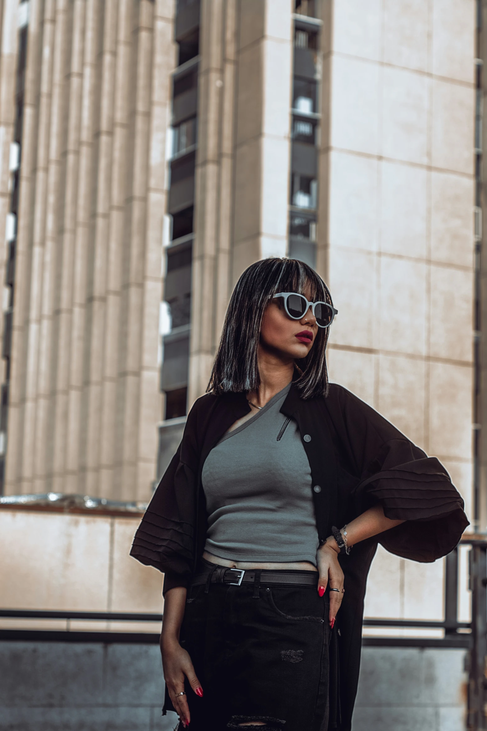 woman with dark hair and sunglasses wearing a brown jacket, black skirt, black tights, and black booties