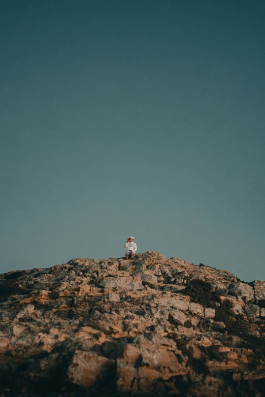 a man sitting on a rock, wearing a jacket