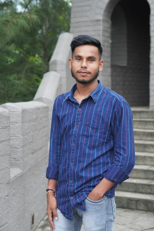 a young man in jeans and a striped shirt standing near steps