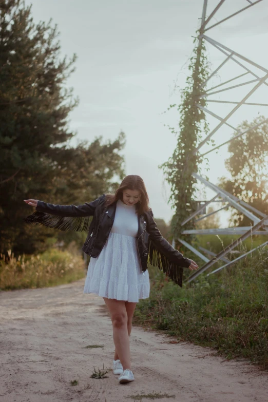 a girl with a jacket on is walking down the dirt road