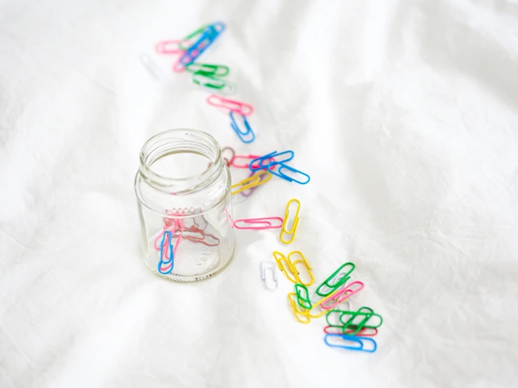 several colored plastic clips sit next to a small glass jar